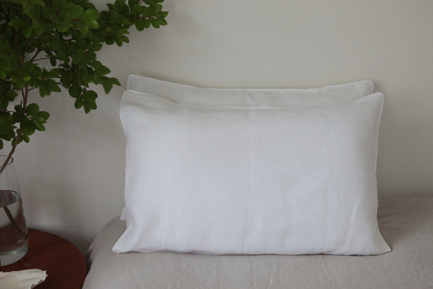 Two stacked white linen pillowcases with white linen piping