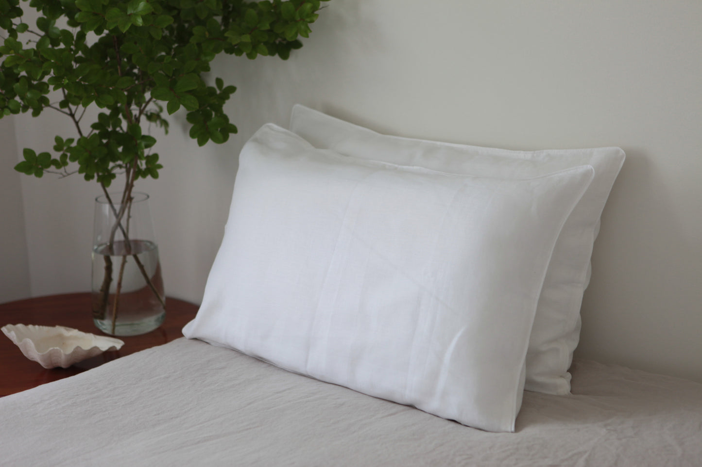 45 degree angle photo of white linen pillow slips with white linen piping.