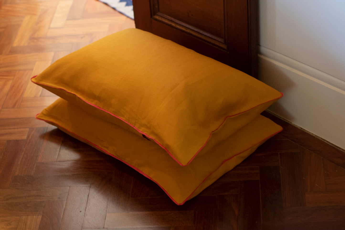 Stacked burnt orange linen pillowcases with hot pink linen piped edge.