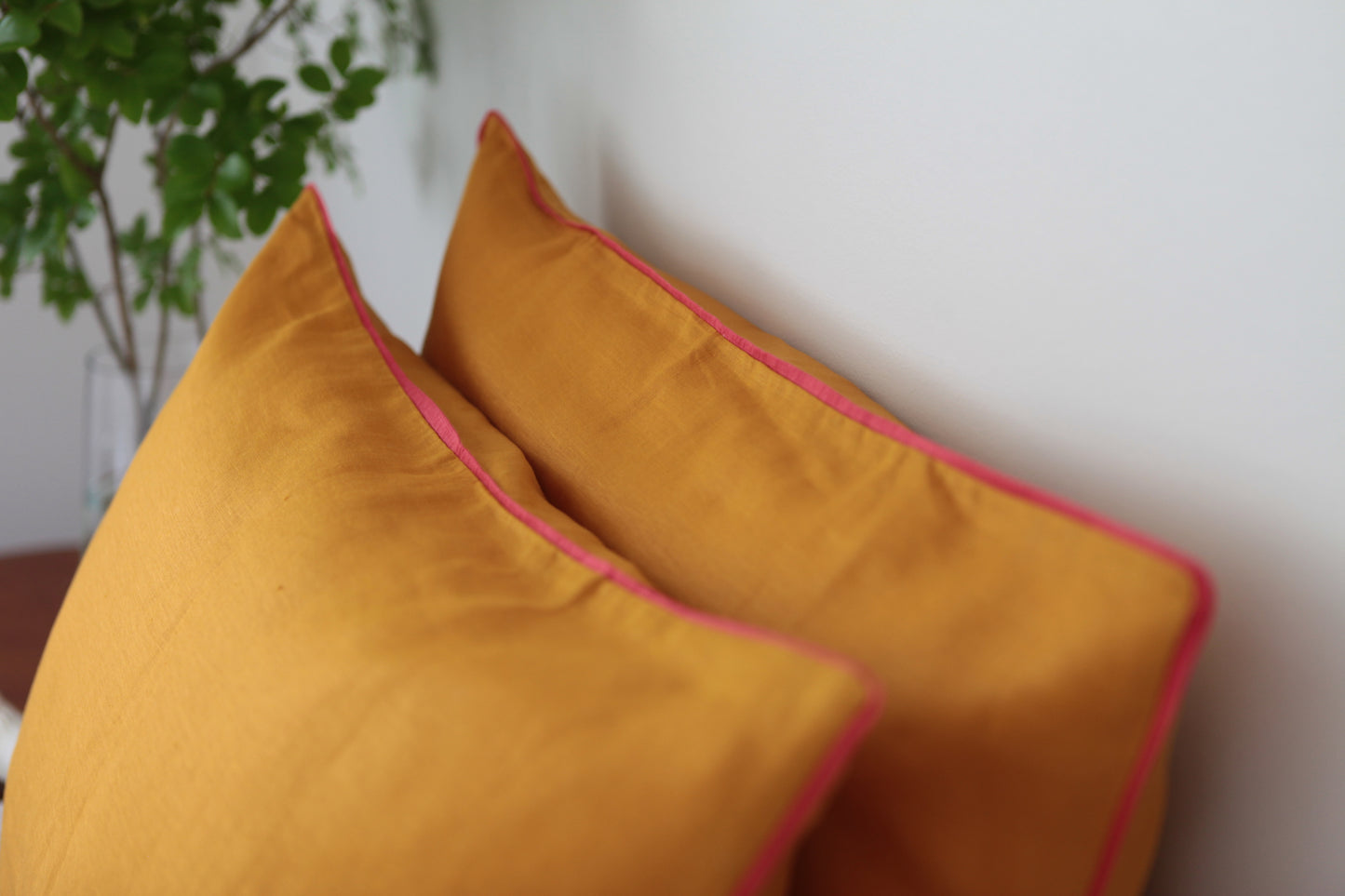 Burnt orange linen pillowcases with magenta linen piping. 45 degree angle photo.