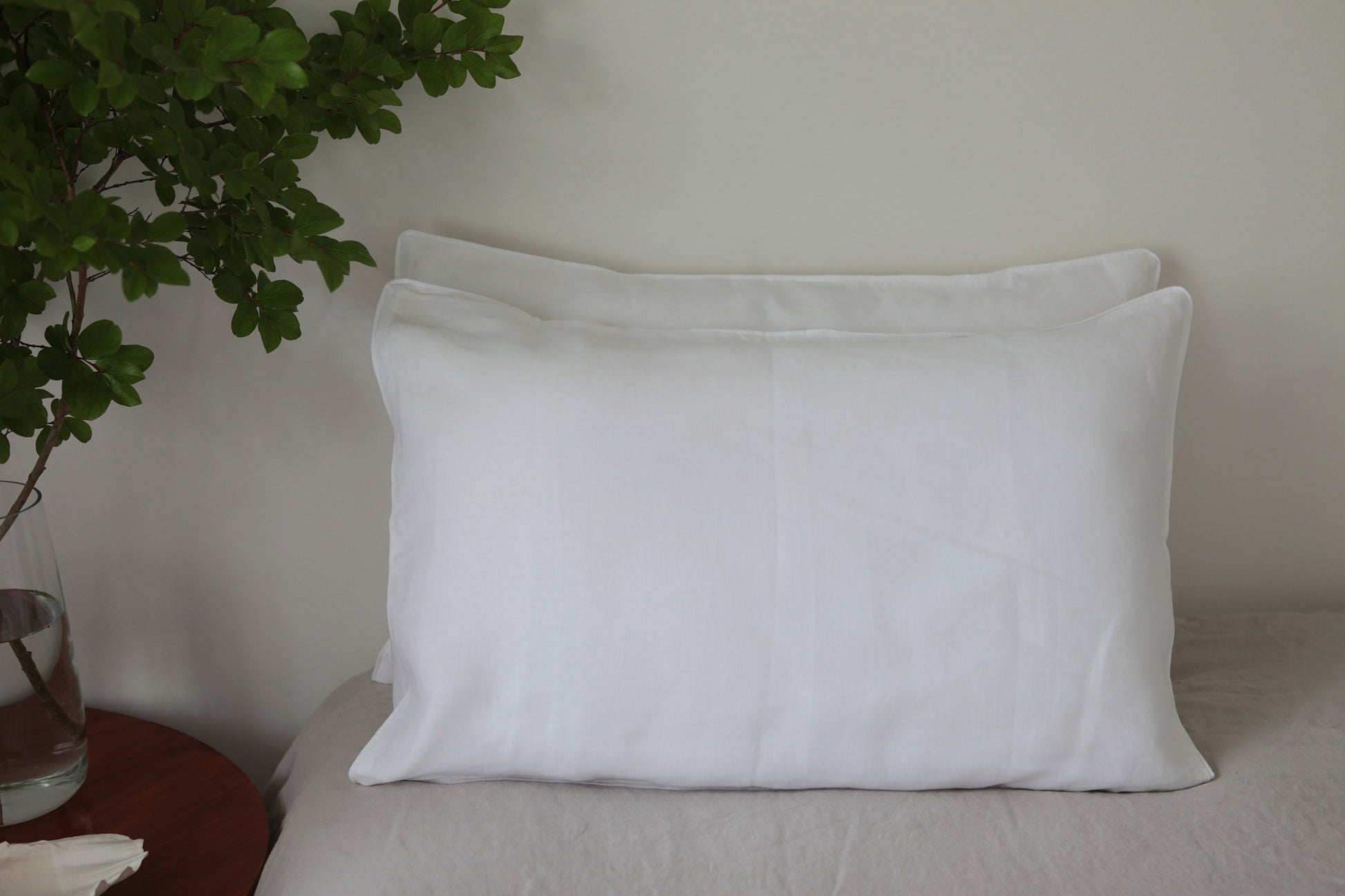 Two stacked white linen pillowcases with white linen piping