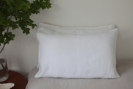 Two stacked white linen pillowcases with white linen piping