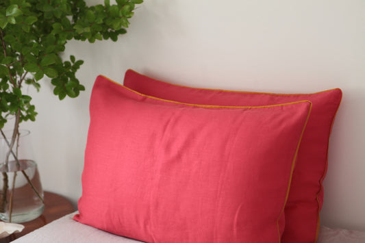 Magenta linen pillowcases with burnt orange piping. Side angle photo. 