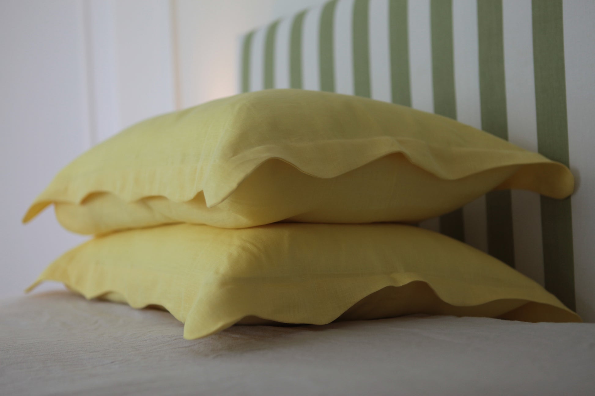 Lemon coloured linen pillowcases with organic wave edge. Photo from corner of stacked pillowcases. 
