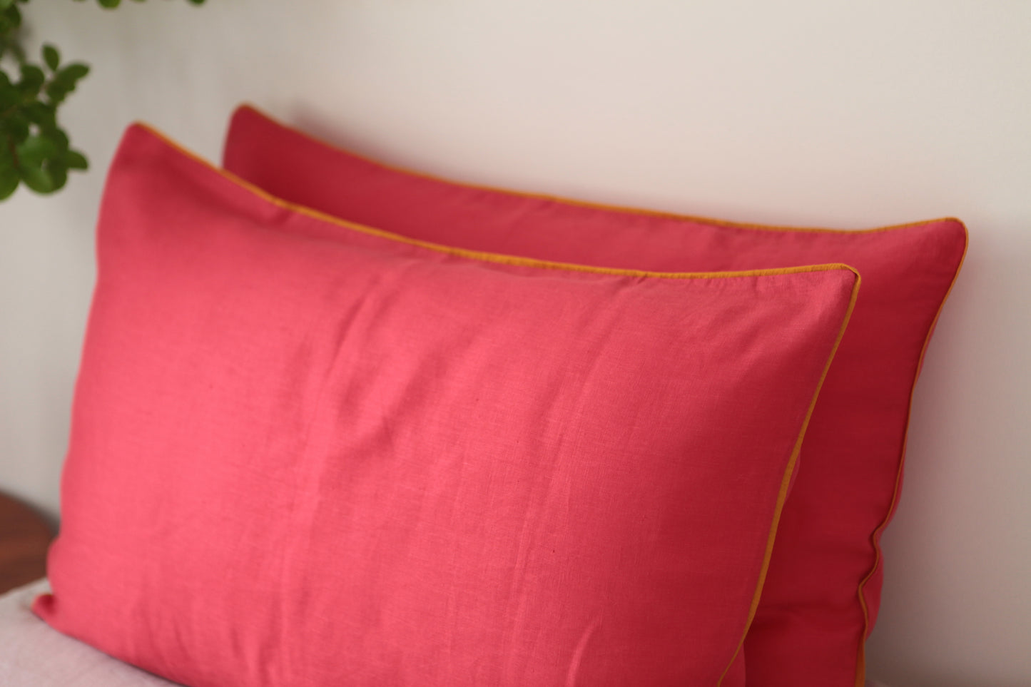 Magenta linen pillowcases with burnt orange linen piping, close up side angle photo.