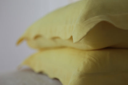 Lemon linen pillowcases stacked. Organic wave edge along border. Out of focus. 