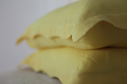 Lemon linen pillowcases stacked. Organic wave edge along border. Out of focus. 