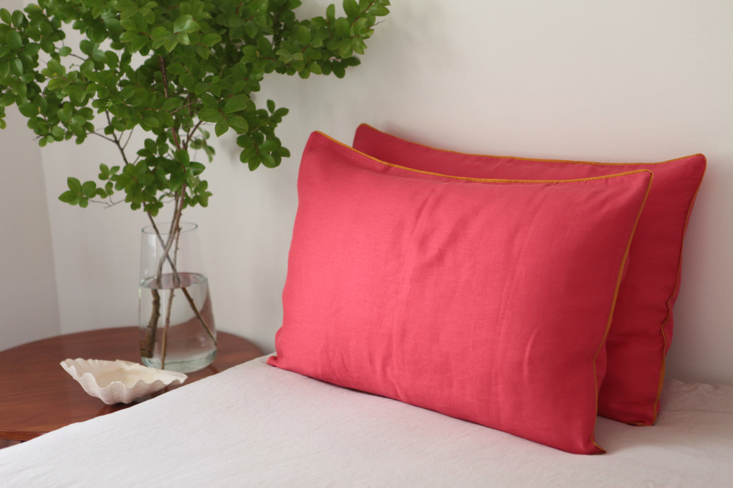 Magenta linen pillowcases with burnt orange linen piping. Studio photo.