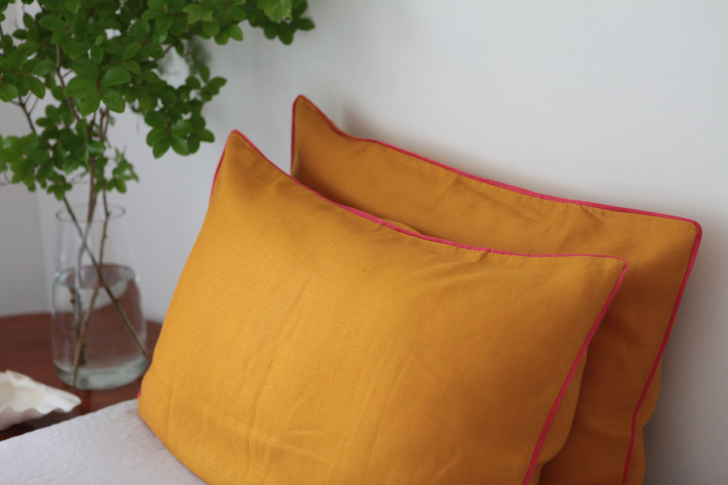 Burnt orange linen pillowcases with magenta linen piping. Side studio photo. 