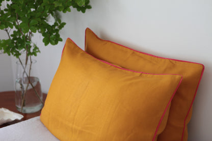 Burnt orange linen pillowcases with magenta linen piping. Side studio photo. 