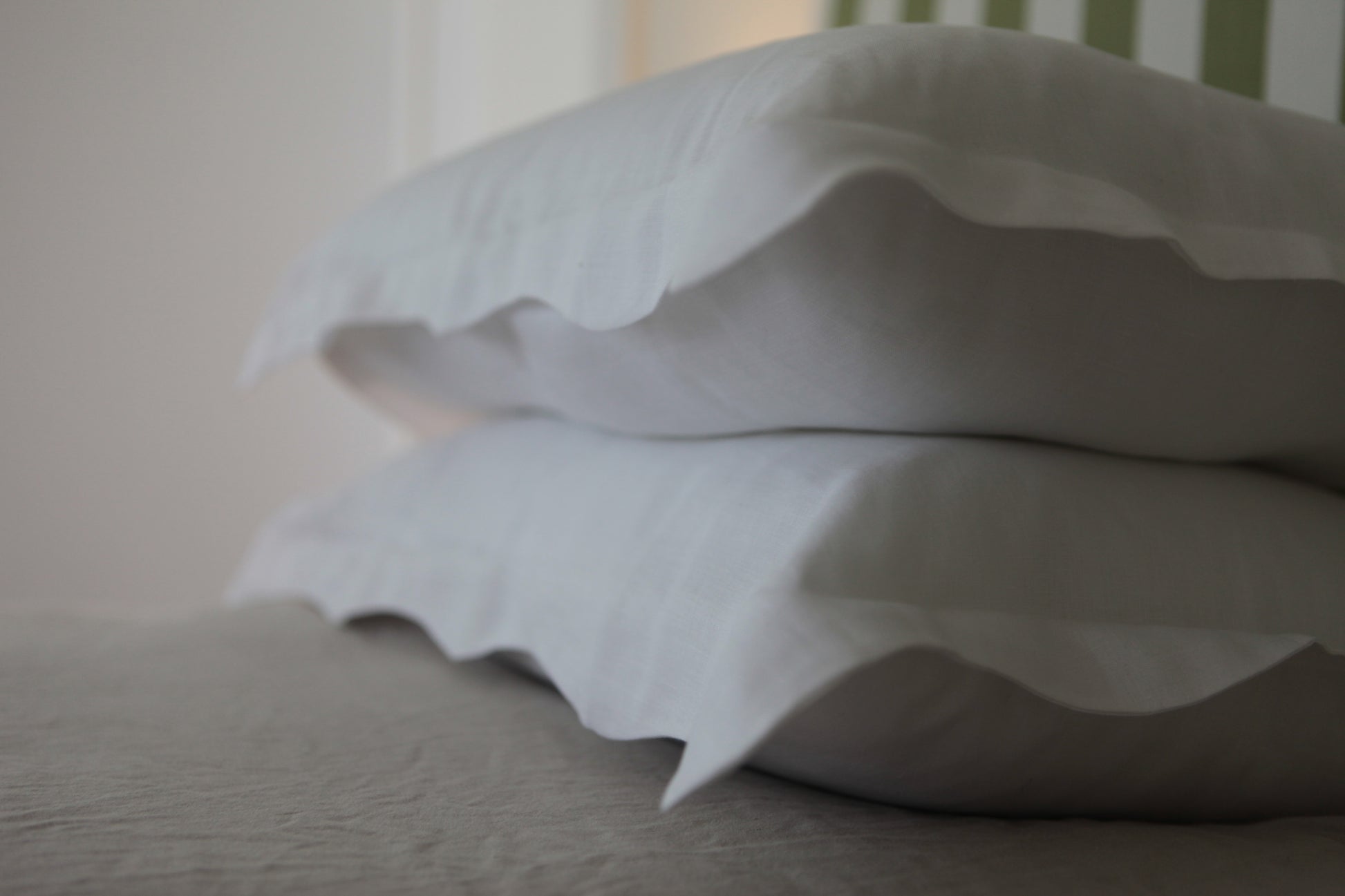 Out of focus image of white linen pillowcases with organic wave edge. 