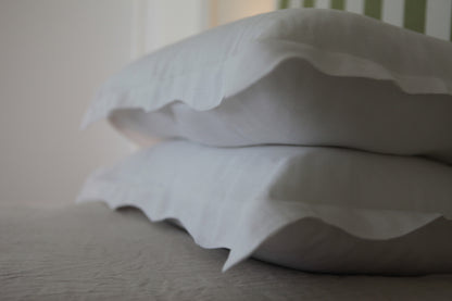 Out of focus image of white linen pillowcases with organic wave edge. 